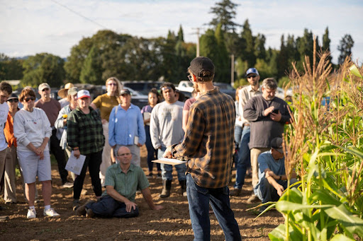 Facilitator speaking to a gathered group in a dry‑farmed field during a field tour.